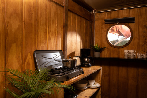 Área de cocina en la tienda safari Dream suite en Holiday Park Mölke con estufa, ventana y vajilla.