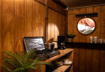 Coin cuisine dans la tente safari Dream suite au Holiday Park Mölke avec réchaud, fenêtre et vaisselle.