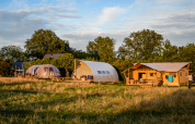 Tre tende da glamping dal design originale su un prato verde, circondate da alberi, al tramonto.