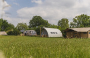 Moderne Campinghütten vor grüner Wiese im Holiday Park Mölke, einschließlich Riverdome und Sanitärbereich.