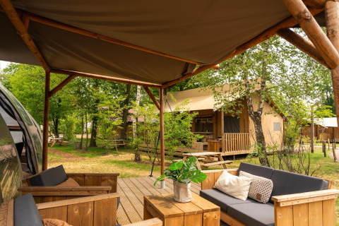 Terraza al aire libre con sofás modernos en Riverdome lodge, frente a cabañas en Holiday Park Mölke, Países Bajos.