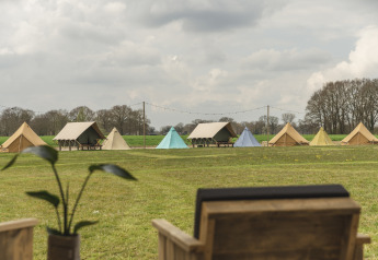 View of multiple tents set up on a grassy field at a lodge, seen from behind a wooden chair on a cloudy day.