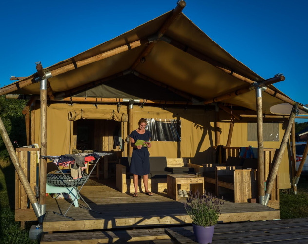Una mujer está de pie en la terraza de una tienda safari con muebles de madera y ropa tendida al sol.