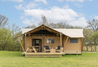 Foto eines Safari-Zeltes mit Holzterrasse, Sitzgelegenheiten und Picknicktisch auf einer Wiese.