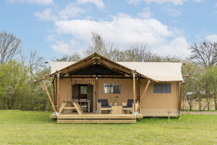 Foto de una tienda safari con terraza de madera, zona de estar exterior y mesa en un campo verde.