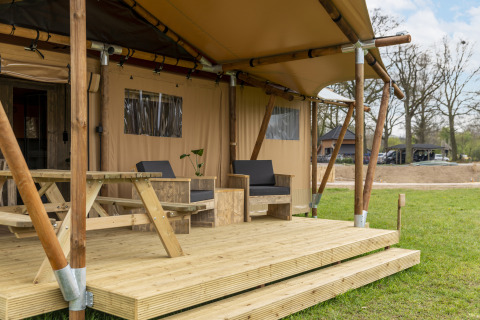 Safari-Zelt mit Holzterrasse, Picknicktisch und Loungestühlen, gelegen auf einer grünen Wiese.