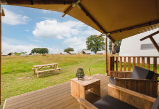 Vista da una veranda di tenda safari con sedie di legno e vino su un campo erboso con altre tende.