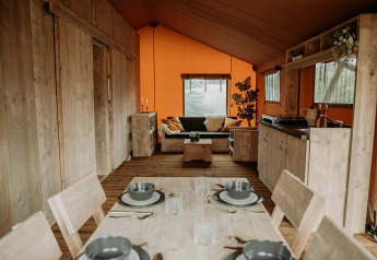 Interieur van een luxe safaritent met houten meubels, eettafel, zithoek en kitchenette.