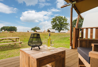 Gezellige safari-tentveranda met wijn, glazen, lantaarn, picknicktafel en tenten op de achtergrond.