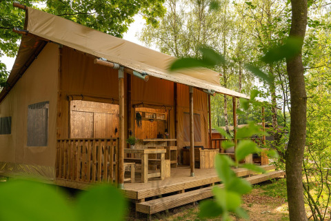 Safari-Zelt 'the bartender' mit Sanitäranlagen im Holiday Park Mölke, Niederlande, von Bäumen umgeben.