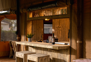 Tenda safari 'the bartender' con bar in legno, bicchieri, bottiglia di vino e pianta a Holiday Park Mölke, Paesi Bassi.