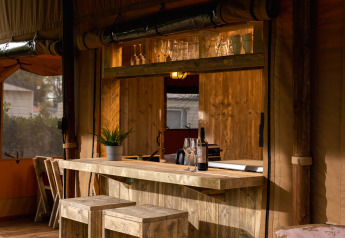 Safari-Zelt 'the bartender' mit Holzbar, Gläsern, Weinflasche und Pflanzen im Holiday Park Mölke, Niederlande.