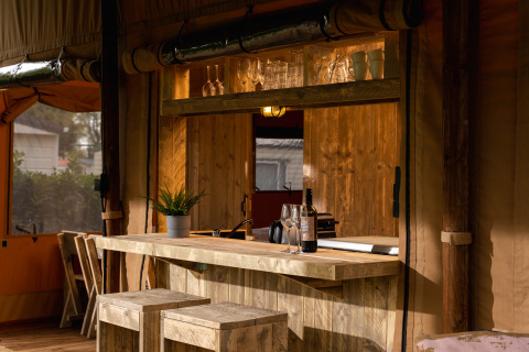 Safari-Zelt 'the bartender' mit Holzbar, Gläsern, Weinflasche und Pflanzen im Holiday Park Mölke, Niederlande.