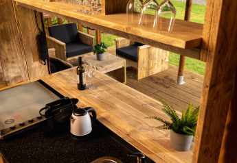 Area interna ed esterna della tenda safari 'the bartender' con mobili in legno, bicchieri e piante.