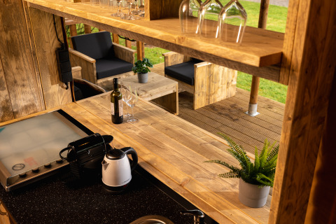 Binnen- en buitenruimte van safaritent 'the bartender' met houten meubilair, glazen en planten.