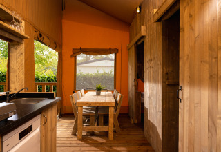 Vista interna della tenda safari 'the bartender' con mobili in legno e cucina a Holiday Park Mölke, Paesi Bassi.