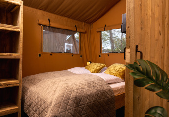 Interieur van safaritent 'the bartender' met gezellig bed en houten plank bij Holiday Park Mölke in Nederland.