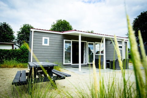 Vista del Dune Lodge en Holiday Park Duinhoeve, Países Bajos, con zona de estar exterior y mesa de picnic.