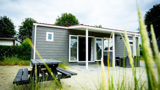 Vista del Dune Lodge en Holiday Park Duinhoeve, Países Bajos, con zona de estar exterior y mesa de picnic.