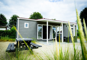 Vista del Dune Lodge en Holiday Park Duinhoeve, Países Bajos, con zona de estar exterior y mesa de picnic.