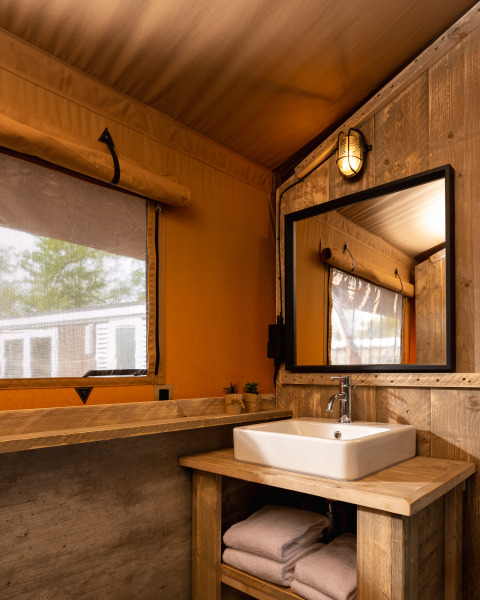 Bagno in tenda safari con lavandino in legno, specchio, asciugamani e luce calda a Holiday Park Mölke.