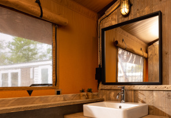 Bagno in tenda safari con lavandino in legno, specchio, asciugamani e luce calda a Holiday Park Mölke.