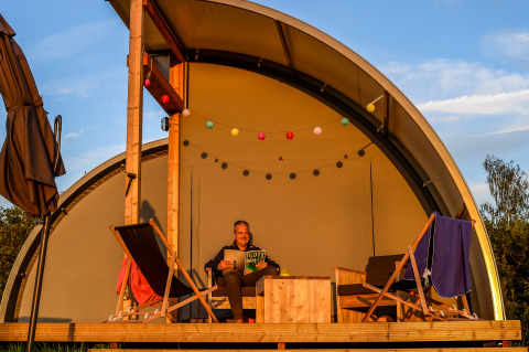 Persoon ontspant op het terras van Panorama Lodge bij Holiday Park Mölke, Nederland, met ligstoelen.