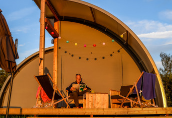 Persoon ontspant op het terras van de Panorama Lodge bij Holiday Park Mölke, Nederland, met ligstoelen.