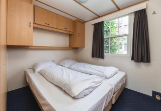 Slaapkamer in Bungalow aan de Regge in Holiday Park Mölke, Nederland, met twee bedden en opbergruimte.