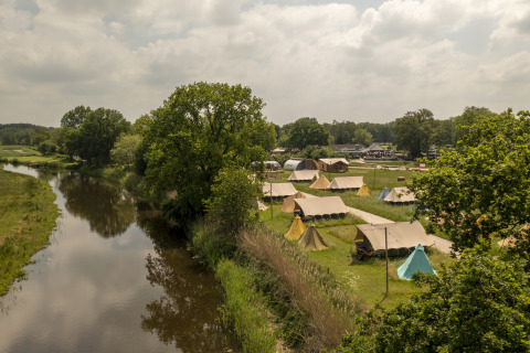 Vue aérienne de tentes safari près d'une rivière au Holiday Park Mölke, Pays-Bas, entourés de verdure.