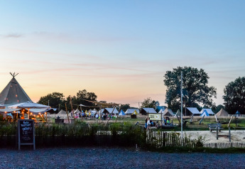 Glamping al tramonto con tende lussuose illuminate, area relax e ospiti che godono l'atmosfera serale.