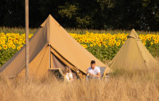 Dos personas descansan frente a una tienda belltent en Holiday Park Mölke, Países Bajos, junto a girasoles.