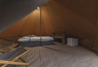 Interior de una tienda tipi con cama, nevera pequeña y sillas en Holiday Park Mölke, Países Bajos.