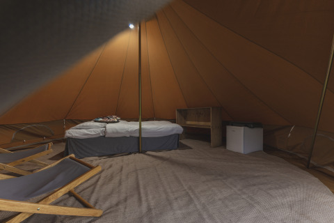 Indersiden af en teepee-telt med seng, minibar og stole på Holiday Park Mölke i Holland.