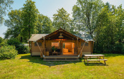 Foto af et rummeligt safari-telt med overdækket terrasse, omgivet af grønne træer og picnicbord foran.
