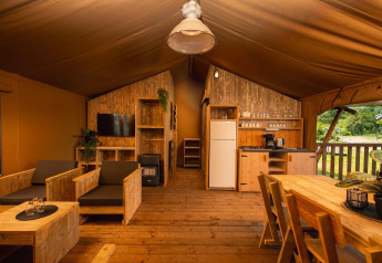 Intérieur d'une tente safari avec meubles en bois, cuisine, salon, table à manger et vue sur la nature.