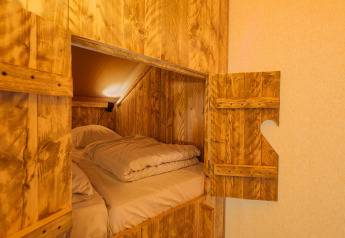 Cozy sleeping pod inside a safari tent with wooden walls, bedding, and an open door showing the interior.
