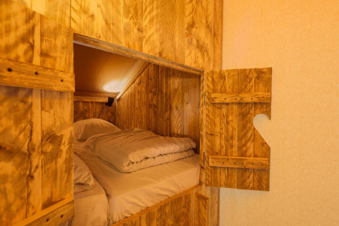 Coin nuit douillet dans une tente safari, murs en bois, literie confortable et porte entrouverte.