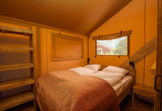 Interior de tienda safari con cama doble, estantería de madera, ventana y luz cálida en el dormitorio.