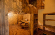Interior de una tienda safari con suelo de madera, mesa, taburetes, estantería y litera con escalera.