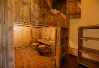 Interior de una tienda safari con suelo de madera, mesa, taburetes, estantería y litera con escalera.
