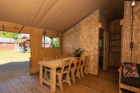 Interieur van een safaritent met houten eetset, stoelen en zicht op het groene buitengebied.