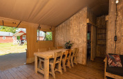 Vista interior de una tienda safari con muebles de madera, mesa de comedor y sillas, con vista al exterior.