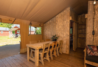 Interieur van een safaritent met houten eetset, stoelen en zicht op het groene buitengebied.