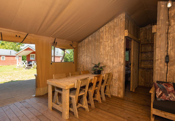 Interieur van een safaritent met houten eetset, stoelen en zicht op het groene buitengebied.