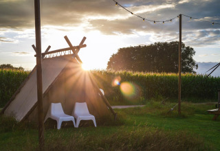 Tienda de glamping al atardecer con dos sillas blancas frente a un campo y luces colgantes encima.