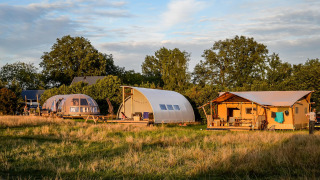 Luxe glamping tenten in Holiday Park Mölke, Nederland, tussen groene velden en bomen bij avondlicht.