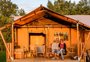Two people relaxing in front of a luxury glamping tent at Holiday Park Mölke in the Netherlands, sunny day.