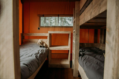 Interior de una tienda de glamping de lujo con literas de madera y ropa de cama gris en Holiday Park Mölke.