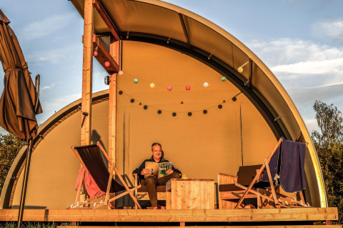 Personne se détendant et lisant dans une tente de glamping de luxe à Holiday Park Mölke, aux Pays-Bas au coucher du soleil.
